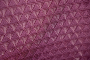Nahaufnahme eines lila Stoffes mit dreieckigem Muster, perspektivisch von der Seite aufgenommen.