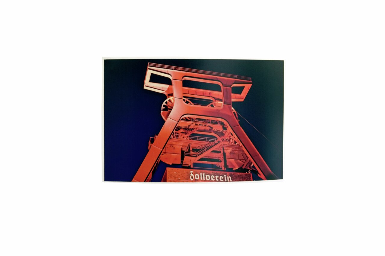 Foto van de verlichte schachttoren van de Zollverein-kolenmijn bij nacht, gefotografeerd vanaf de grond.