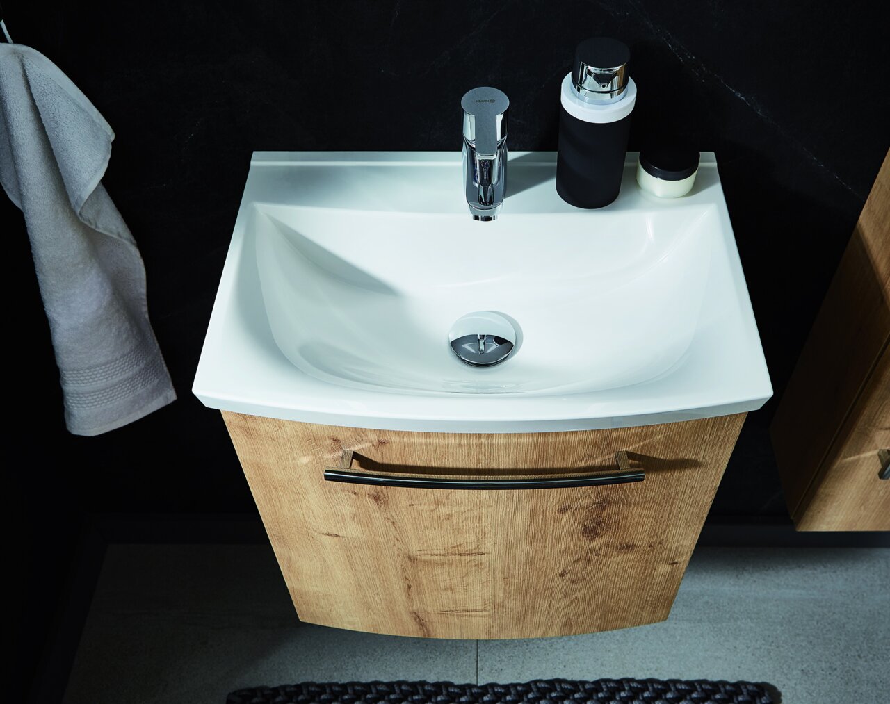 Waschbecken mit Holzunterschrank, von oben fotografiert, mit Handtuch und Accessoires.