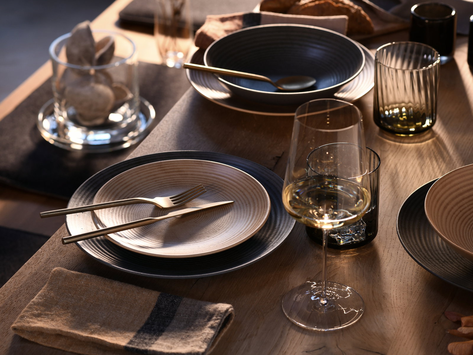 Elegantes Tellerset 18-tlg auf einem gedeckten Tisch, mit goldfarbenem Besteck und Weinglas, aus der Vogelperspektive betrachtet.