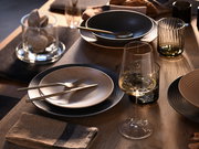 Elegantes Tellerset 18-tlg auf einem gedeckten Tisch, mit goldfarbenem Besteck und Weinglas, aus der Vogelperspektive betrachtet.