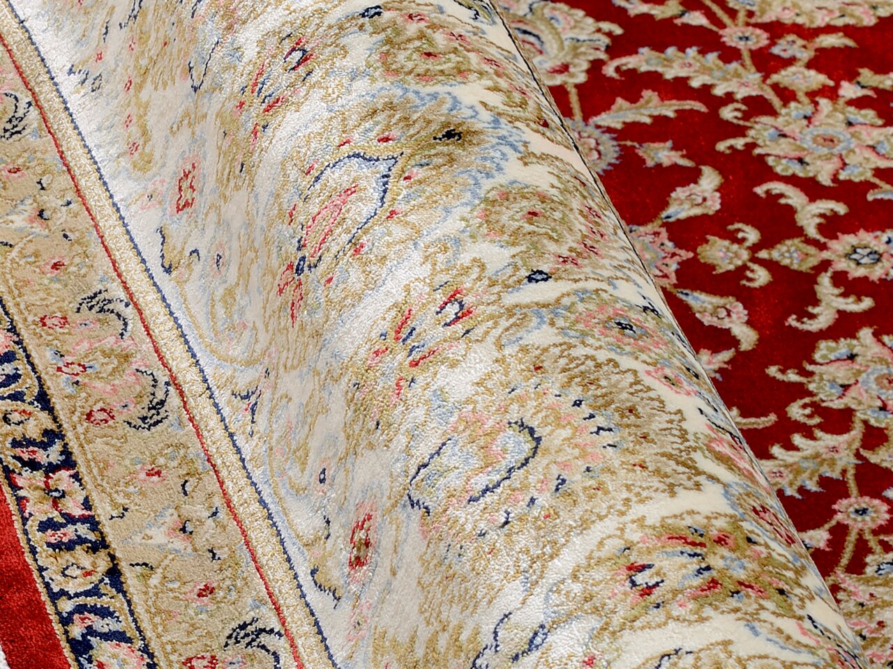 Nahaufnahme eines Orientteppichs mit floralem Muster in Rot, Beige und Blau, teilweise aufgerollt.