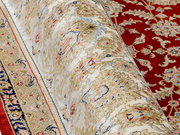 Nahaufnahme eines Orientteppichs mit floralem Muster in Rot, Beige und Blau, teilweise aufgerollt.