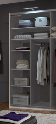 Ein geöffneter Kleiderschrank mit mehreren Regalböden, auf denen gefaltete Kleidung und Boxen liegen, sowie einer Kleiderstange mit hängenden Hemden. Die Perspektive zeigt den Schrank von vorne.