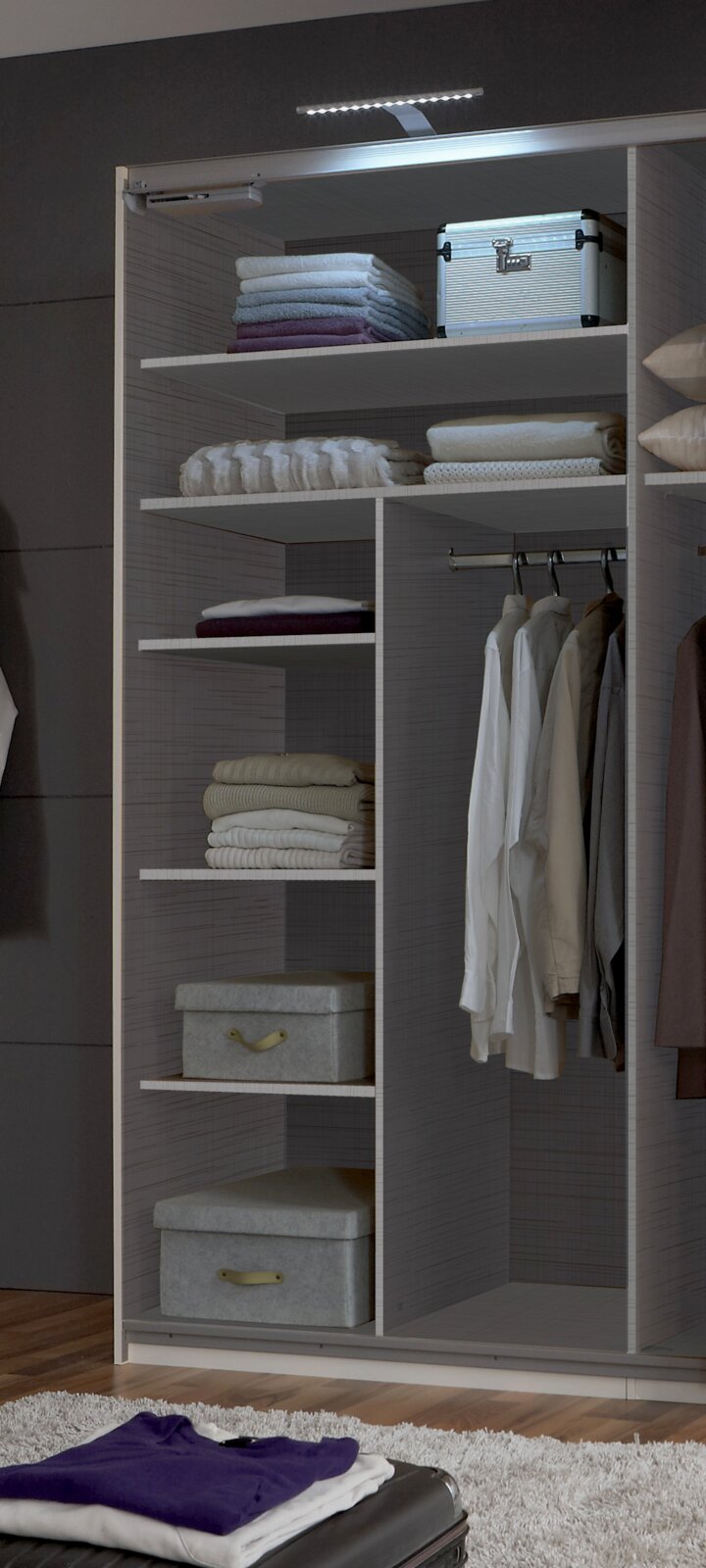 Ein geöffneter Kleiderschrank mit mehreren Regalböden, auf denen gefaltete Kleidung und Boxen liegen, sowie einer Kleiderstange mit hängenden Hemden. Die Perspektive zeigt den Schrank von vorne.