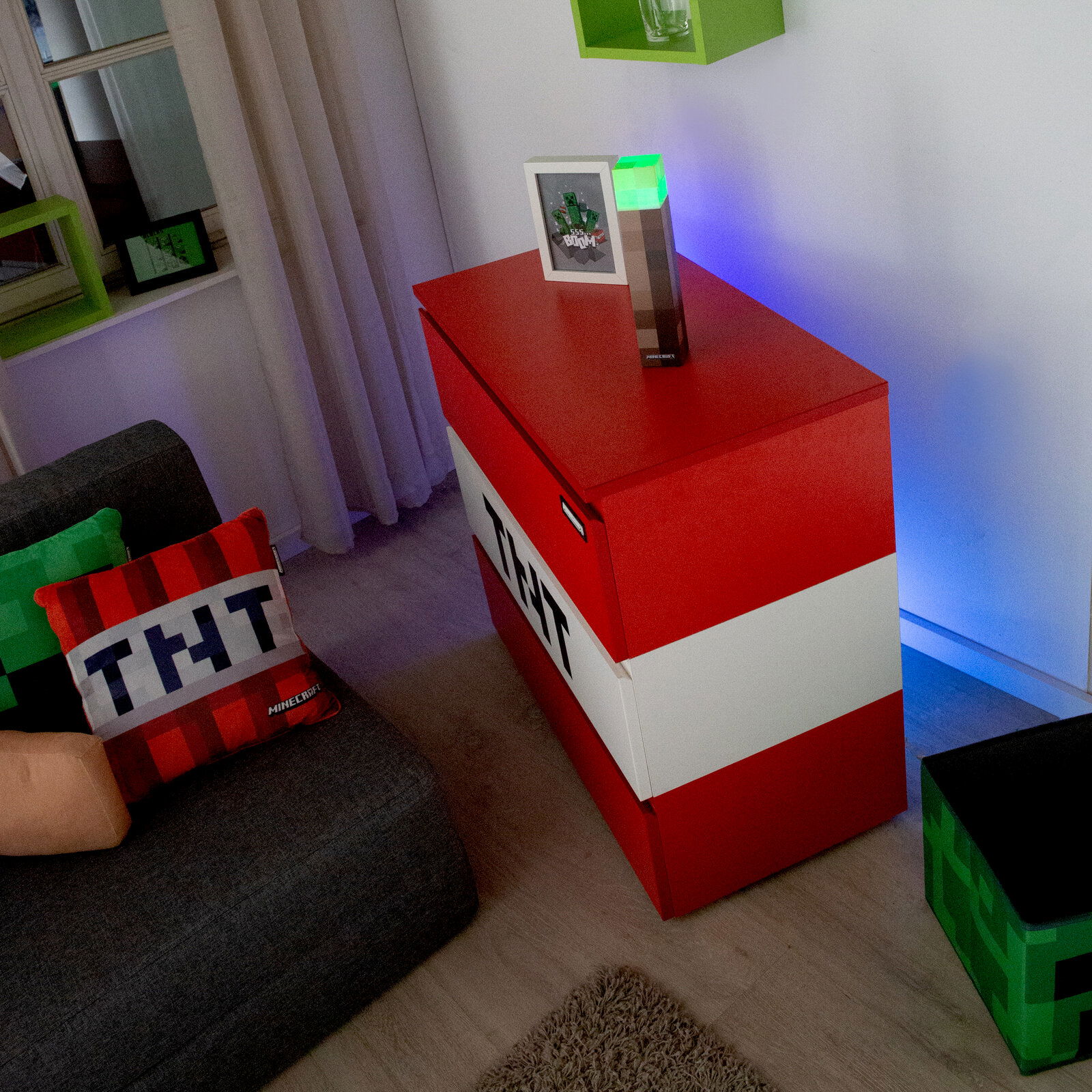 Rote und weiße Minecraft-TNT-Aufbewahrungsbox/Truhe im Wohnzimmer, schräg von oben aus der Ecke fotografiert; oben steht eine leuchtende Minecraft-Redstone-Fackel-Lampe neben einem gerahmten Bild.