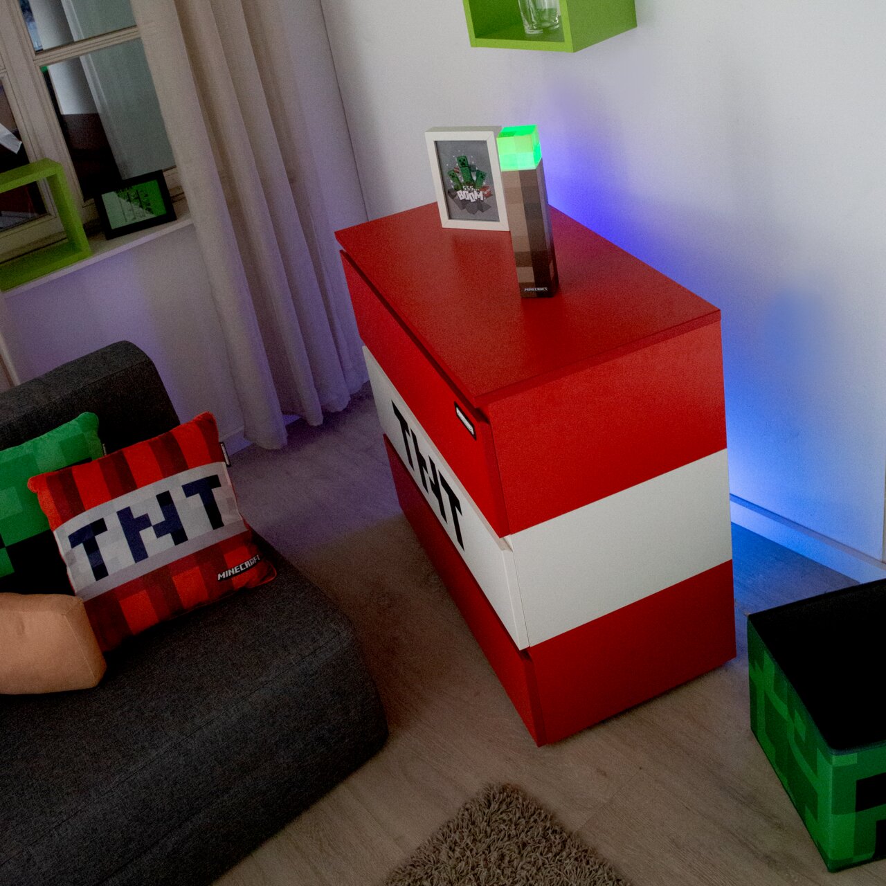 Een rode en witte Minecraft-TNT-opbergdoos/kist in de woonkamer, schuin van bovenaf vanuit de hoek gefotografeerd; bovenop staat een brandende Minecraft-Redstone-fakkel naast een ingelijste foto.