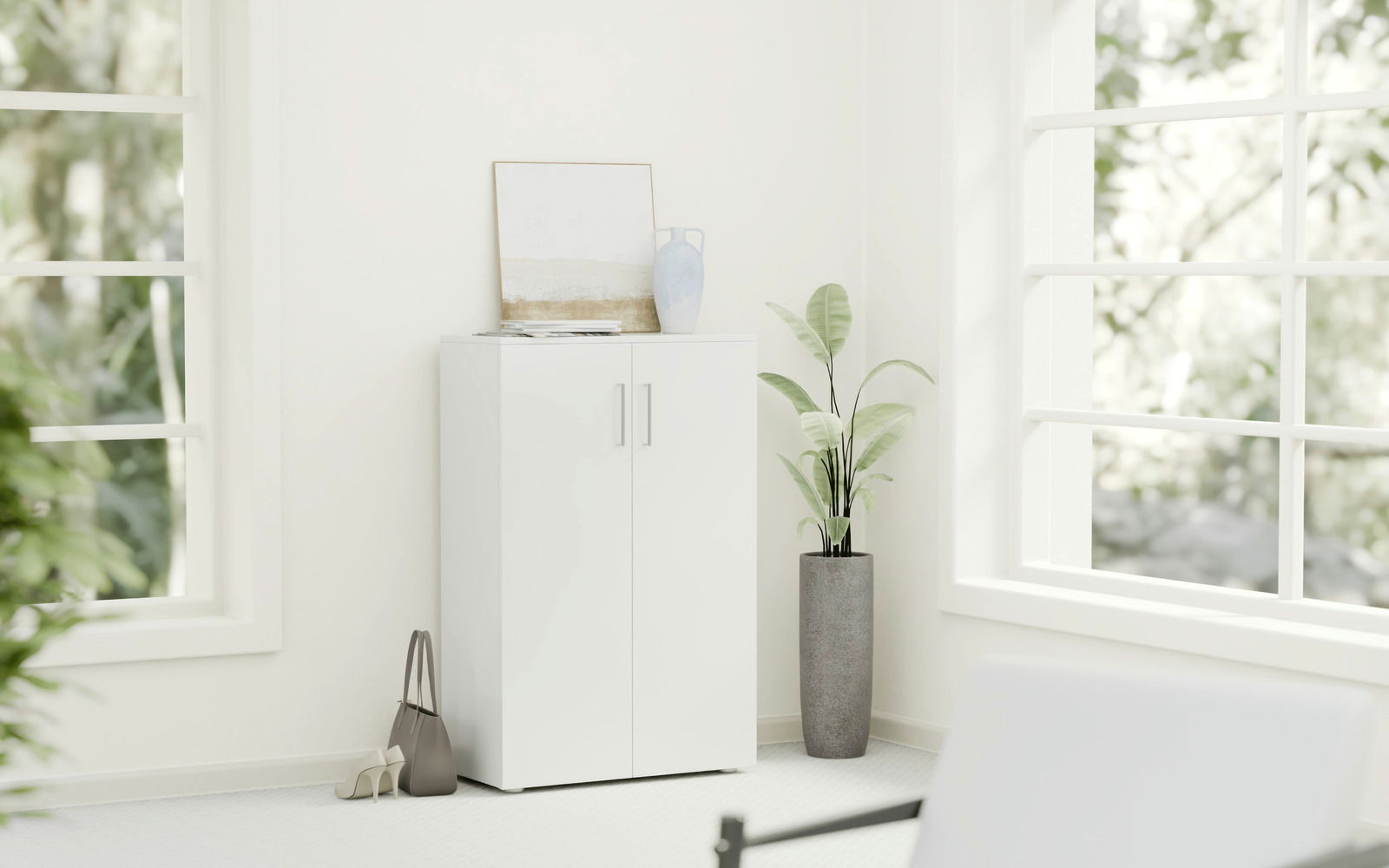 Weißer, niedriger Schuhschrank mit zwei Türen, dekoriert mit einer Vase und einem Bild, in einem hellen Raum mit großen Fenstern, seitliche Perspektive.