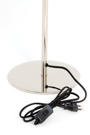 Close-up van de voet van een tafellamp met een glanzende metalen voet en een zwarte kabel met schakelaar.