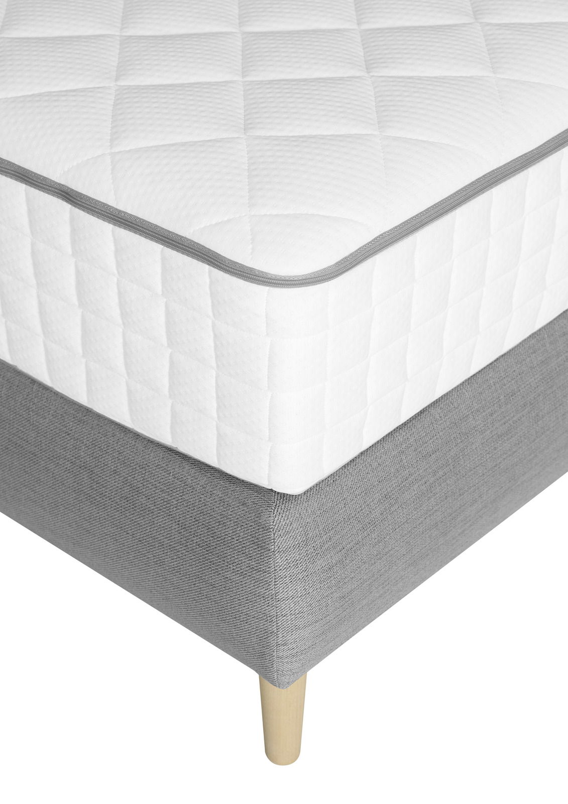 Nahaufnahme eines Boxspringbetts mit weißer, gesteppten Matratze und grauem Unterbau auf Holzfüßen, Perspektive von der Ecke.