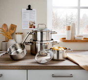 4-delige Charm-pannenset van roestvrij staal, bestaande uit drie pannen en een steelpan, op een aanrecht voor een raam met een winters uitzicht. Perspectief: vooraanzicht.