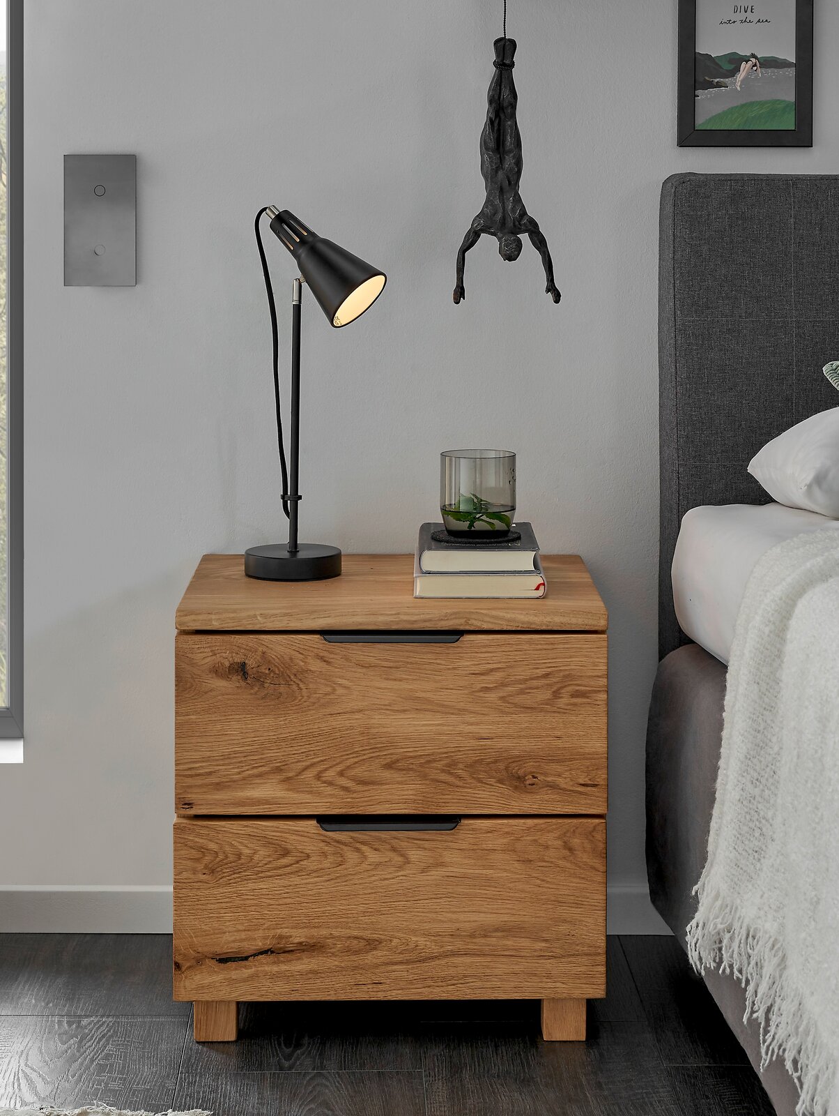 Nachtkommode aus Holz mit zwei Schubladen, darauf eine schwarze Lampe und Bücher, seitliche Perspektive