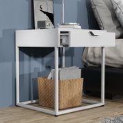 Weißer Nachttisch/Beistelltisch im modernen Design mit Metallgestell und halb geöffneter Schublade, seitliche Frontansicht aus leicht niedriger Perspektive neben einem Bett.