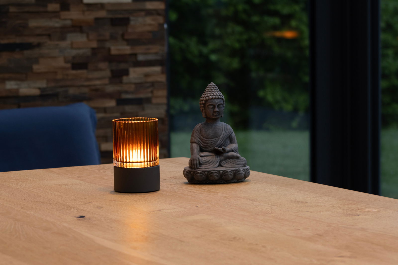 Akku-Windlicht auf einem Holztisch neben einer Buddha-Statue, mit warmem Licht in einem modernen Raum.