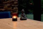 Akku-Windlicht auf einem Holztisch neben einer Buddha-Statue, mit warmem Licht in einem modernen Raum.