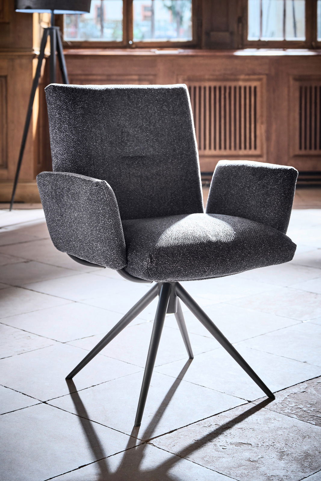 Moderner Armlehnstuhl mit grauem Stoffbezug und schwarzem Metallgestell, seitliche Perspektive.