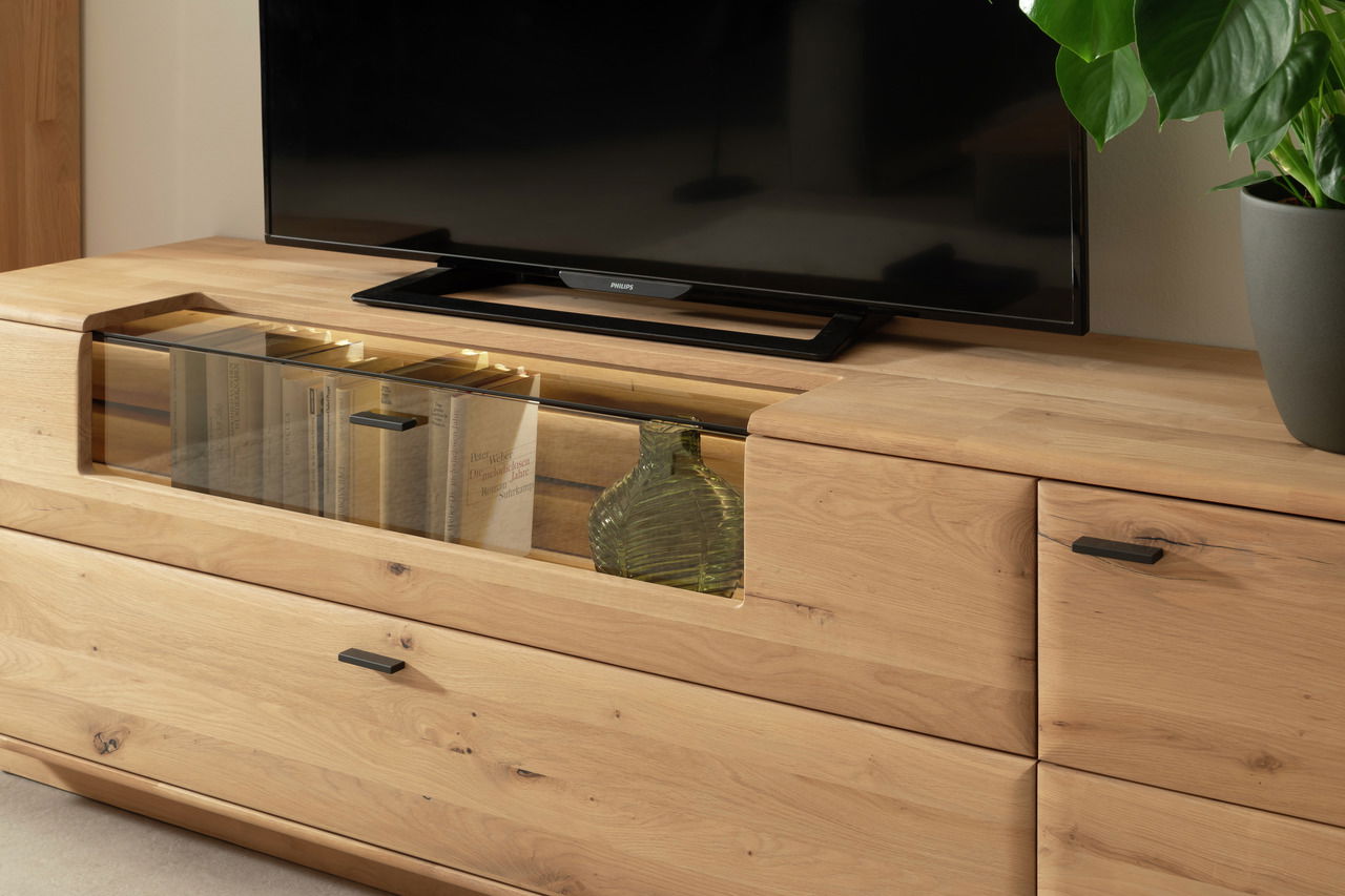 Holz-Lowboard GEORGIA von Linea Natura mit Glasfach, Bücher und Vase, TV darauf, seitliche Perspektive