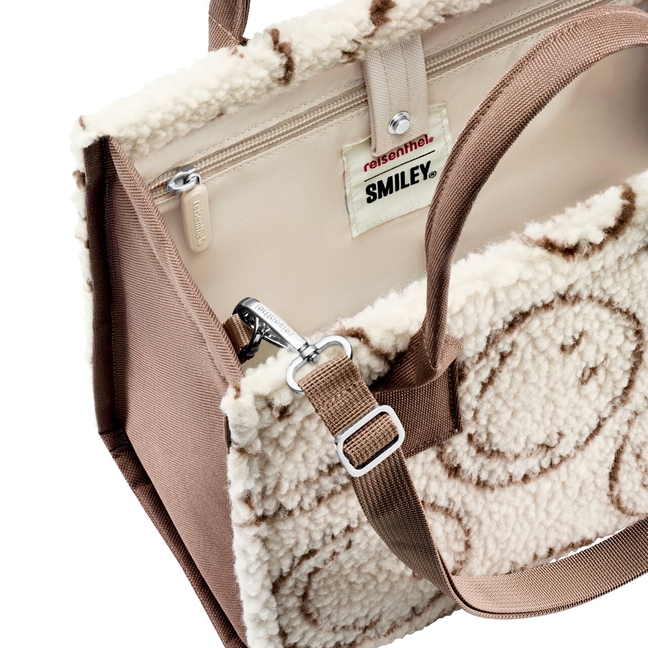 Nahaufnahme einer flauschigen Reisenthel SMILEY Handtasche in Creme mit braunem Muster, braunen Tragegriffen und Reißverschluss, schräg von oben in 3/4-Perspektive gezeigt