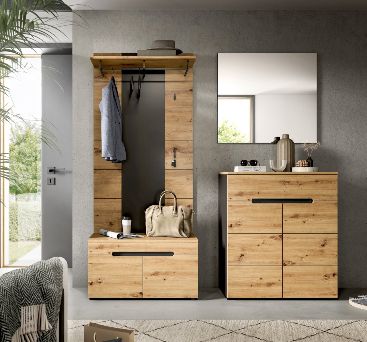 Frontalansicht einer modernen Garderobenkombination aus hellem Holz mit schwarzem Paneel, Hutablage und Haken sowie passender Kommode und Wandspiegel im Flur
