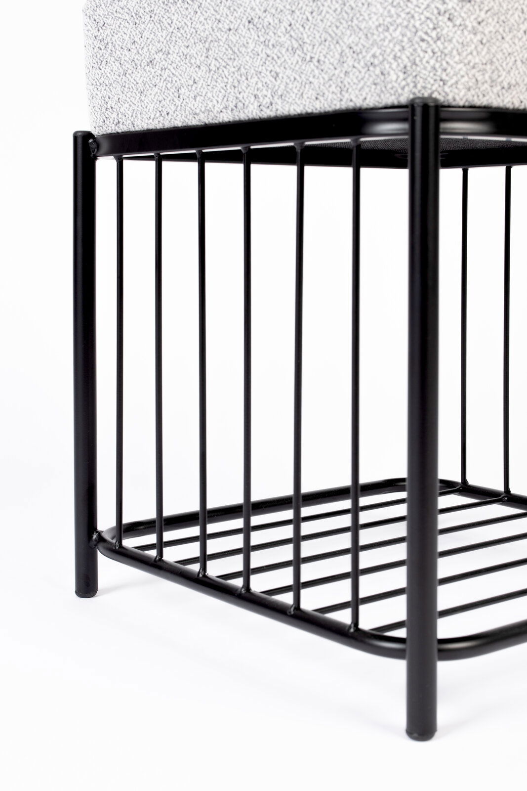 Nahaufnahme eines Hockers mit schwarzem Metallgestell und gepolsterter Sitzfläche, seitliche Perspektive.