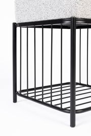 Nahaufnahme eines Hockers mit schwarzem Metallgestell und gepolsterter Sitzfläche, seitliche Perspektive.