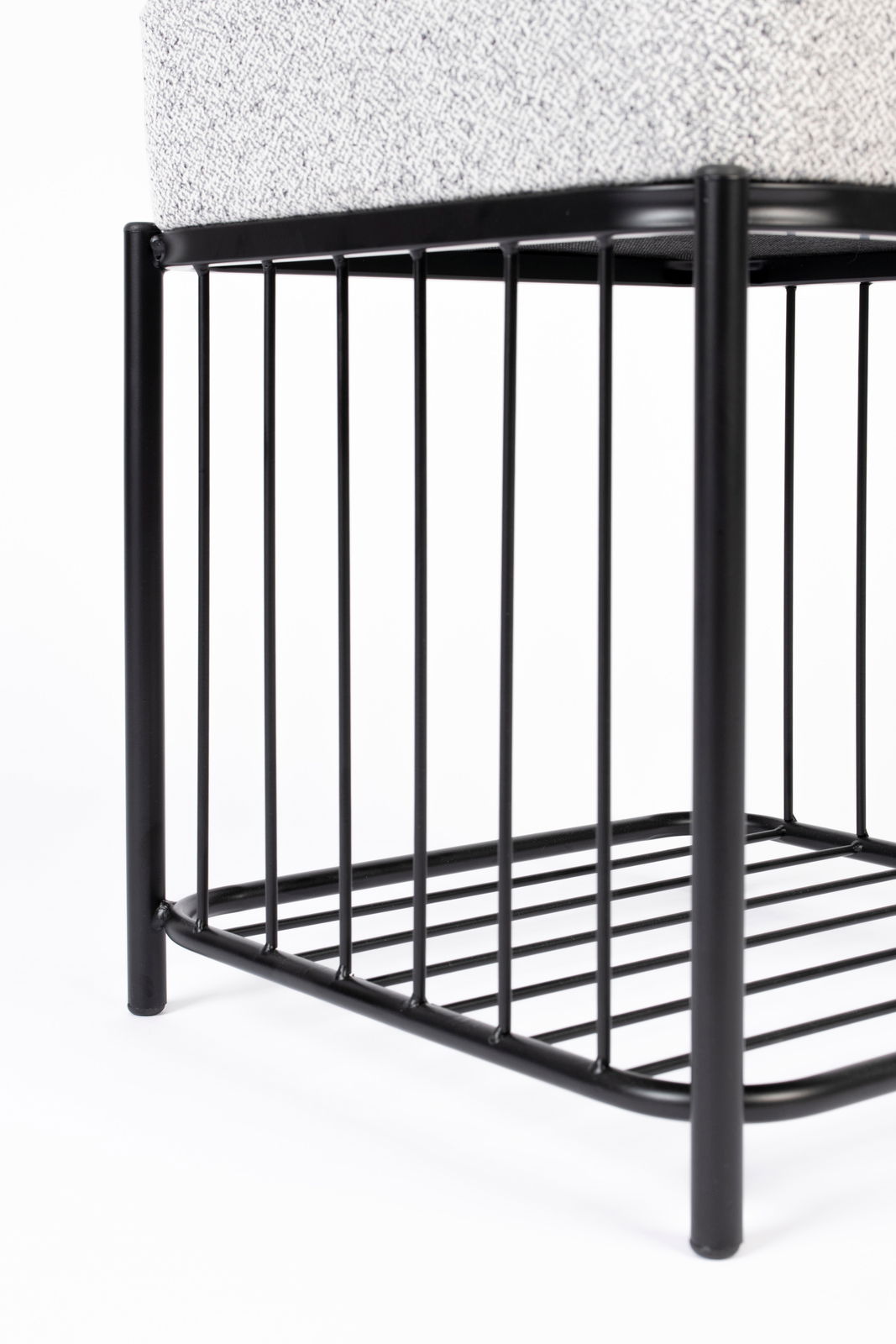 Nahaufnahme eines Hockers mit schwarzem Metallgestell und gepolsterter Sitzfläche, seitliche Perspektive.