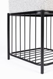 Close-up van een kruk met een zwart metalen frame en een gestoffeerde zitting, gezien vanaf de zijkant.