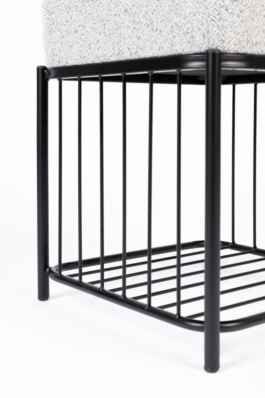 Close-up van een kruk met een zwart metalen frame en een gestoffeerde zitting, gezien vanaf de zijkant.