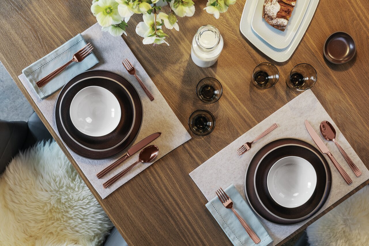 Elegante 30-delige bestekset Cortina in koper, van bovenaf gefotografeerd op een stijlvol gedekte tafel, met bruine borden en witte schalen.