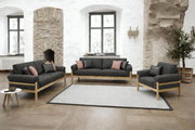 Wohnzimmer-Set mit dunkelgrauem Stoffsofa, passendem Zweisitzer und Sessel auf hellen Holzgestellen, dekoriert mit Kissen, in heller Loft-Umgebung; Perspektive: frontale, leicht erhöhte Weitwinkelansicht