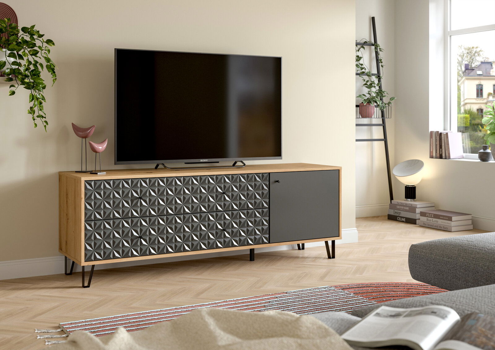 Modernes TV-Lowboard aus hellem Holz mit geometrisch gemusterter Front und grauer Tür auf schwarzen Metallfüßen, im Wohnzimmer mit Fernseher darauf, Perspektive: frontale leicht schräge Ansicht von links.