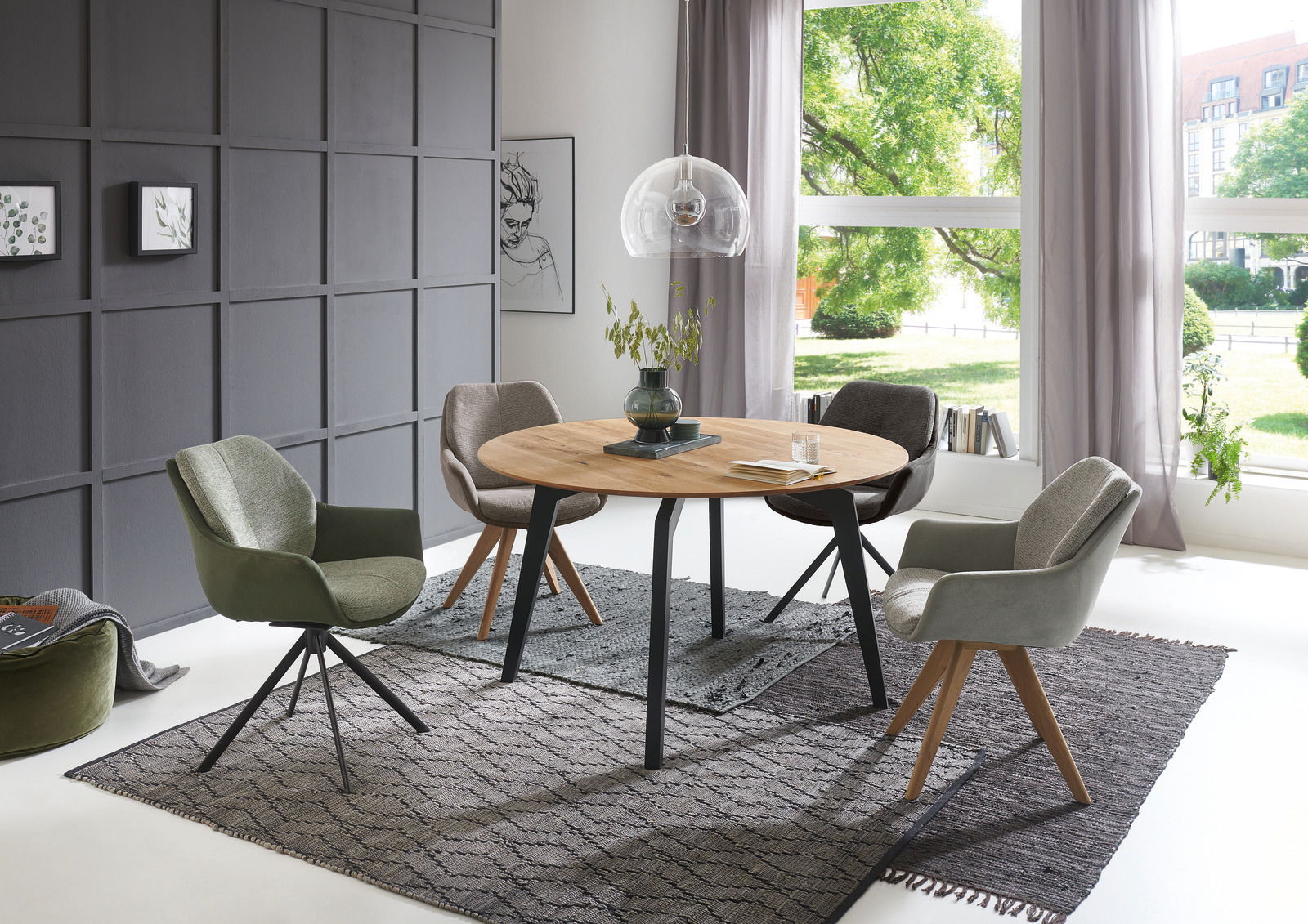 Runder Esstisch mit Holzplatte und schwarzen Metallbeinen, umgeben von vier gepolsterten Stühlen in einem modernen Esszimmer mit großen Fenstern und grauer Wand. Perspektive: seitlich.