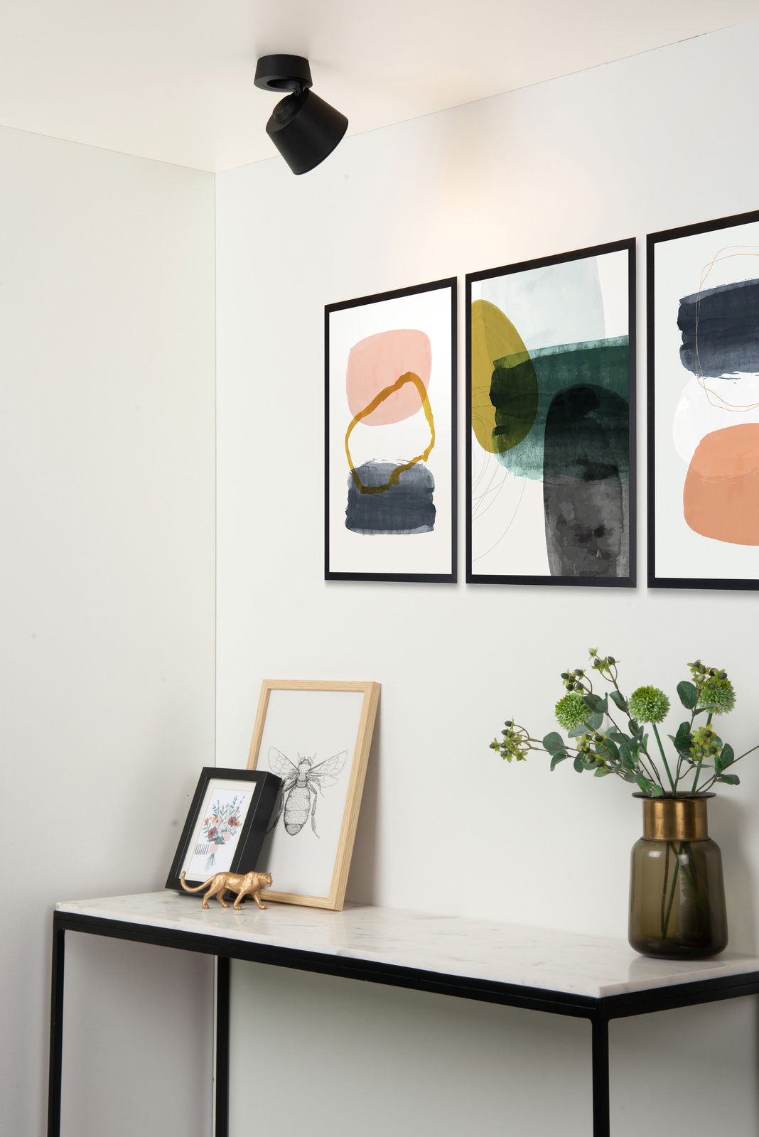 Schwarzer Deckenstrahler in modernem Raum, von unten betrachtet, beleuchtet Wandkunst und Dekoration auf einem Tisch.