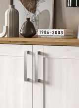 Nahaufnahme einer modernen Kommode mit hellen Holzfronten und silbernen Griffen, dekoriert mit Vasen und Büchern auf der Oberseite.