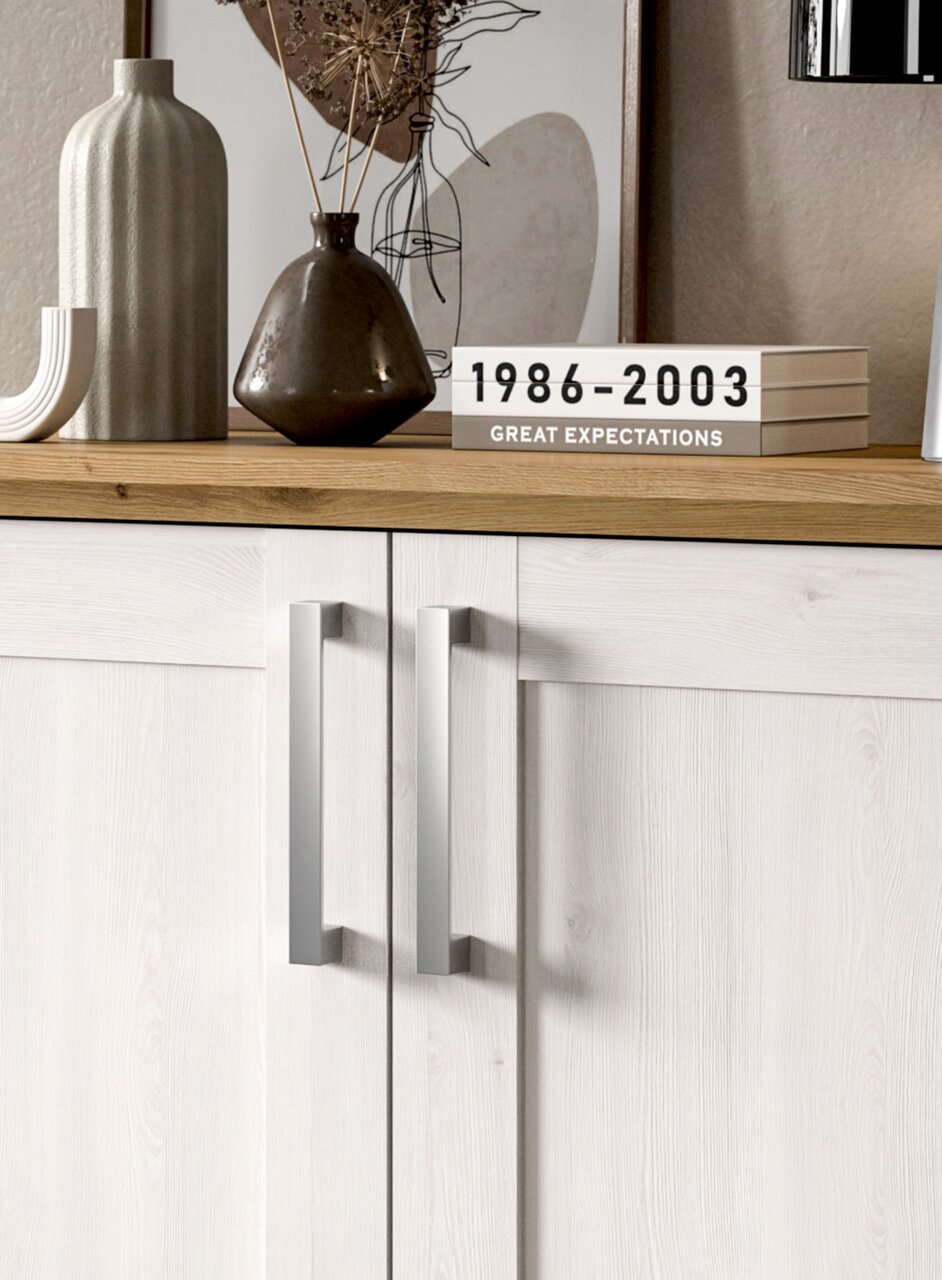 Nahaufnahme einer modernen Kommode mit hellen Holzfronten und silbernen Griffen, dekoriert mit Vasen und Büchern auf der Oberseite.