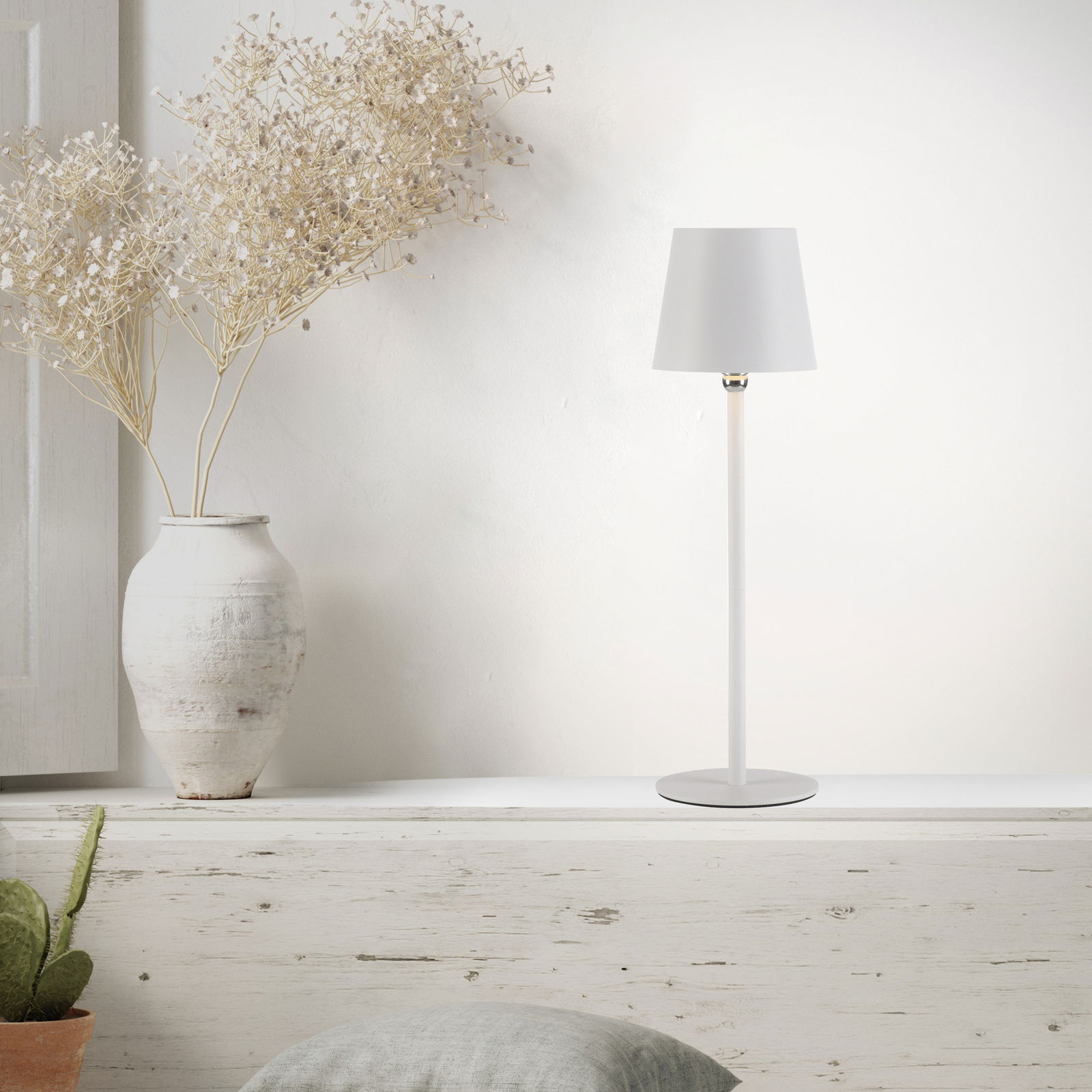 Moderne Akku-Tischleuchte BOTERIA in Weiß, seitliche Perspektive, auf einem rustikalen Regal neben einer Vase mit Trockenblumen.