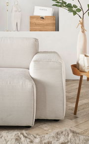 Nahaufnahme einer modernen, hellen Rundecke mit geripptem Stoffbezug, von der Seite betrachtet. Im Hintergrund sind eine Vase mit Zweigen und ein Beistelltisch zu sehen.