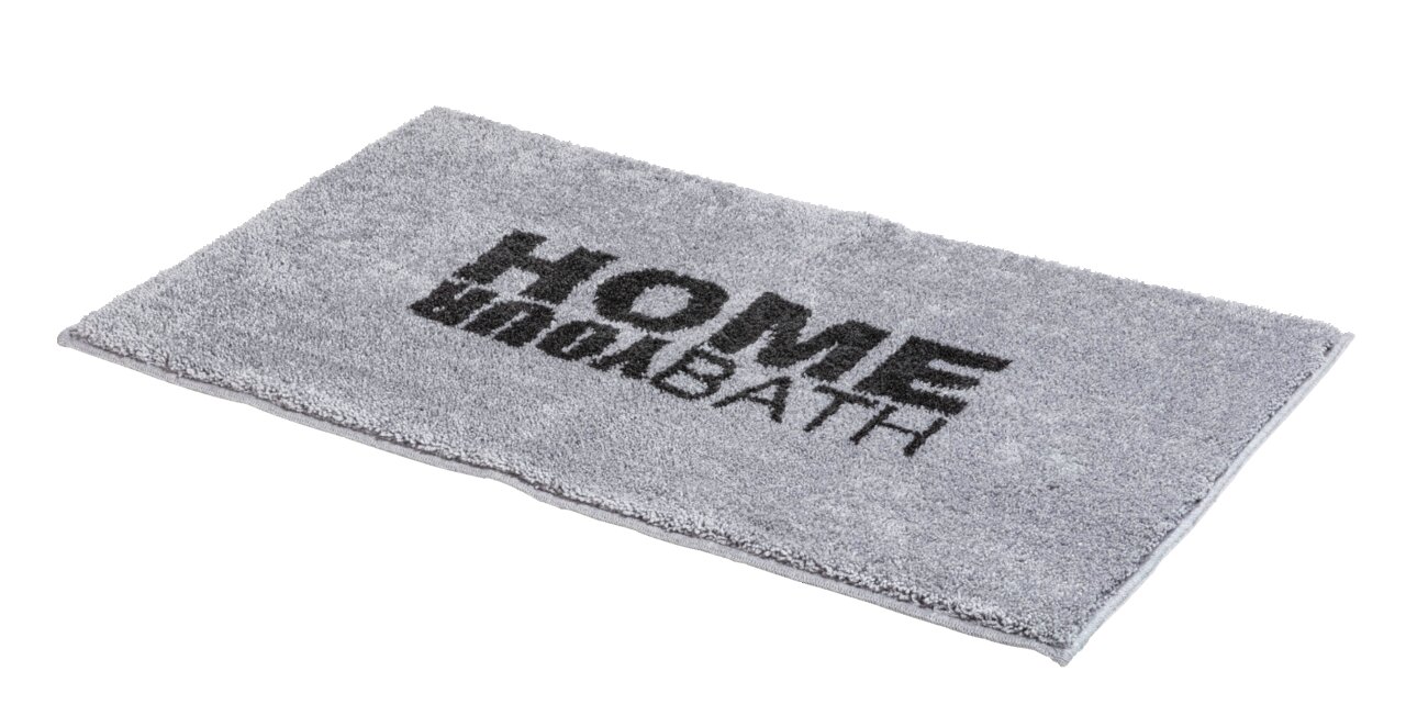 Grauer rechteckiger Badteppich mit der Aufschrift 'HOME BATH' in schwarzer Schrift, perspektivisch von der Seite fotografiert.