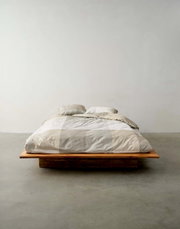 Bed met beddengoed in neutrale tinten, gefotografeerd vanuit het vooraanzicht in een minimalistische ruimte.
