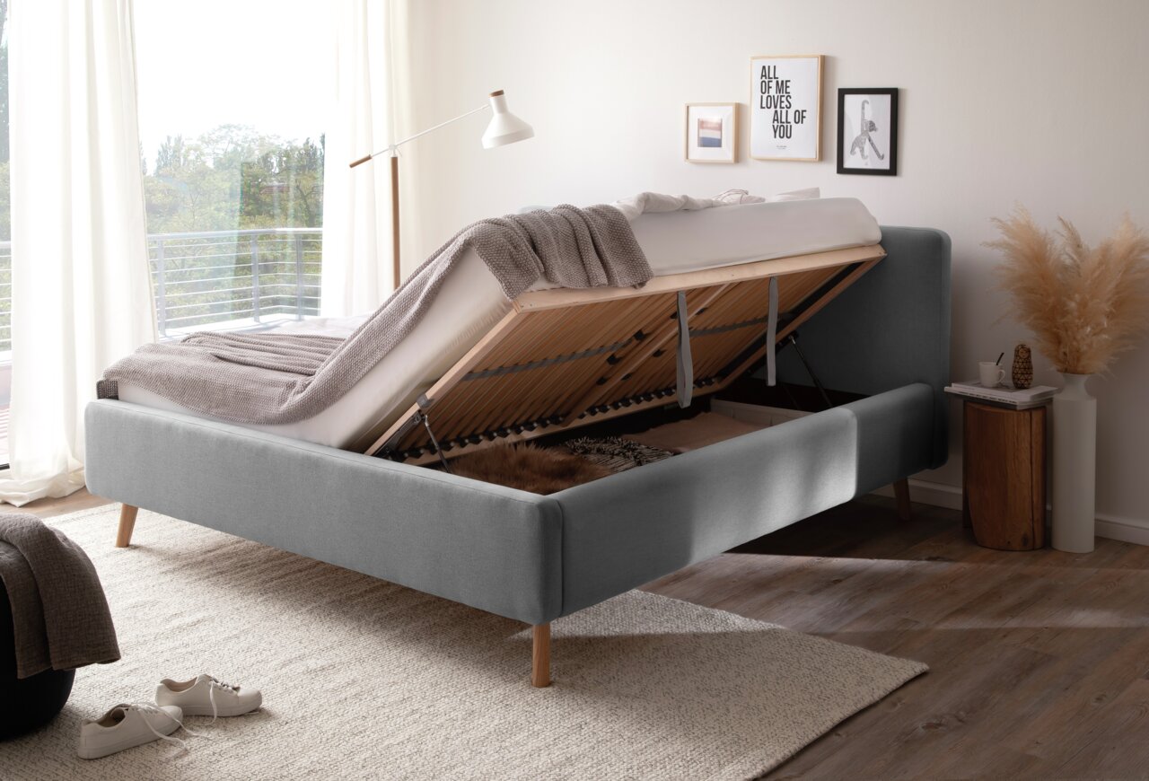 Graues Polsterbett mit hochgeklappter Matratze und Stauraum, seitliche Perspektive