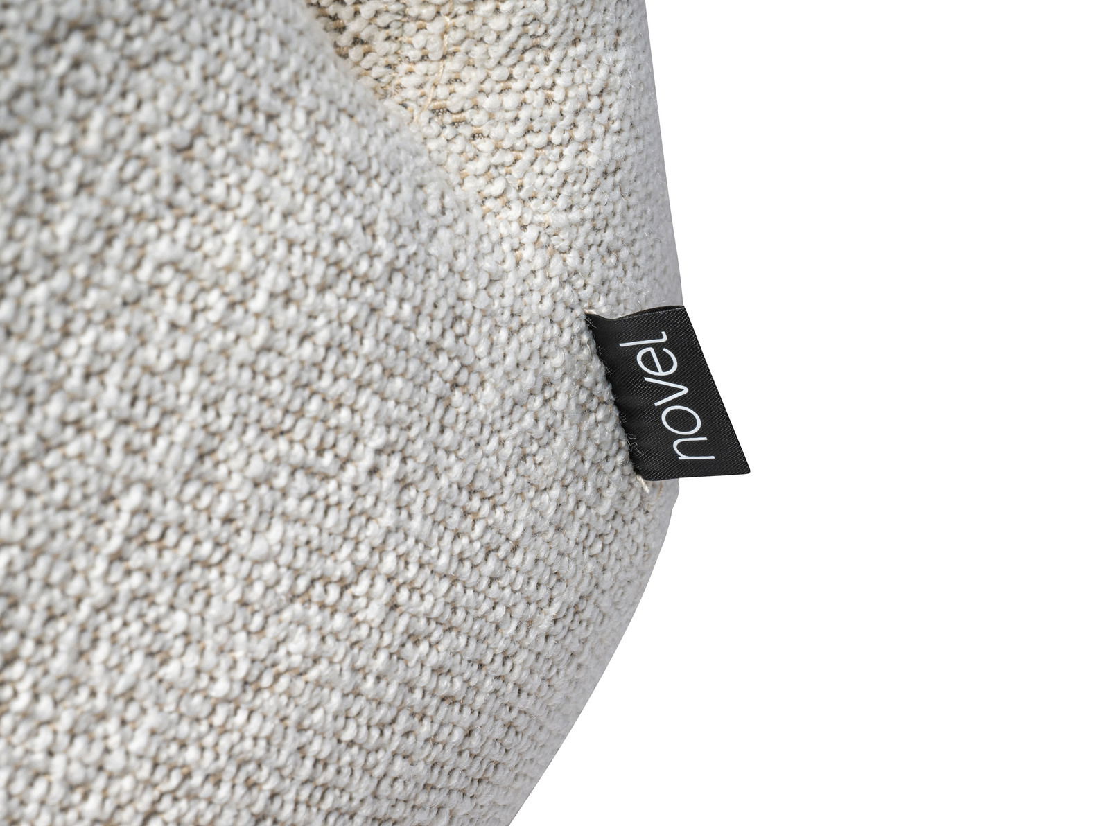Nahaufnahme eines Sessels mit grob gewebtem, cremefarbenem Stoff und einem schwarzen Etikett mit der Aufschrift 'novel'.