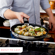 Mann hält eine Pfanne mit Gemüse und Käse über einem Herd, seitliche Perspektive