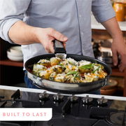 Mann hält eine Pfanne mit Gemüse und Käse über einem Herd, seitliche Perspektive