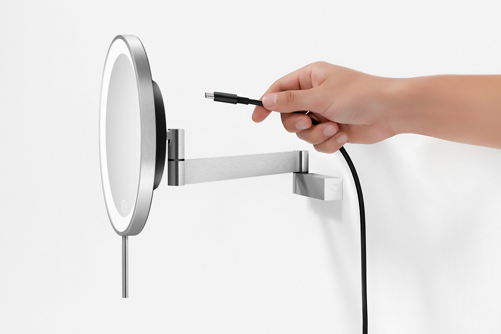 Wandmontierter runder LED-Kosmetikspiegel aus gebürstetem Edelstahl mit ausziehbarem Arm, Seitenansicht; Hand hält USB-Ladekabel vor dem Spiegel auf weißem Hintergrund.