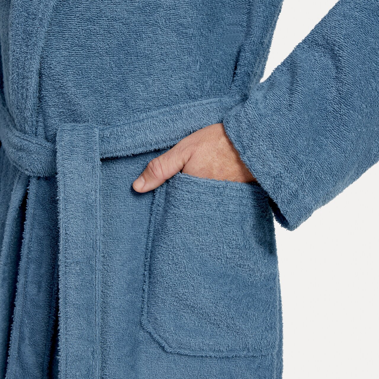 Nahaufnahme eines blauen Bademantels mit Schalkragen in Größe L, zeigt eine Hand in der Tasche und den Gürtel um die Taille.