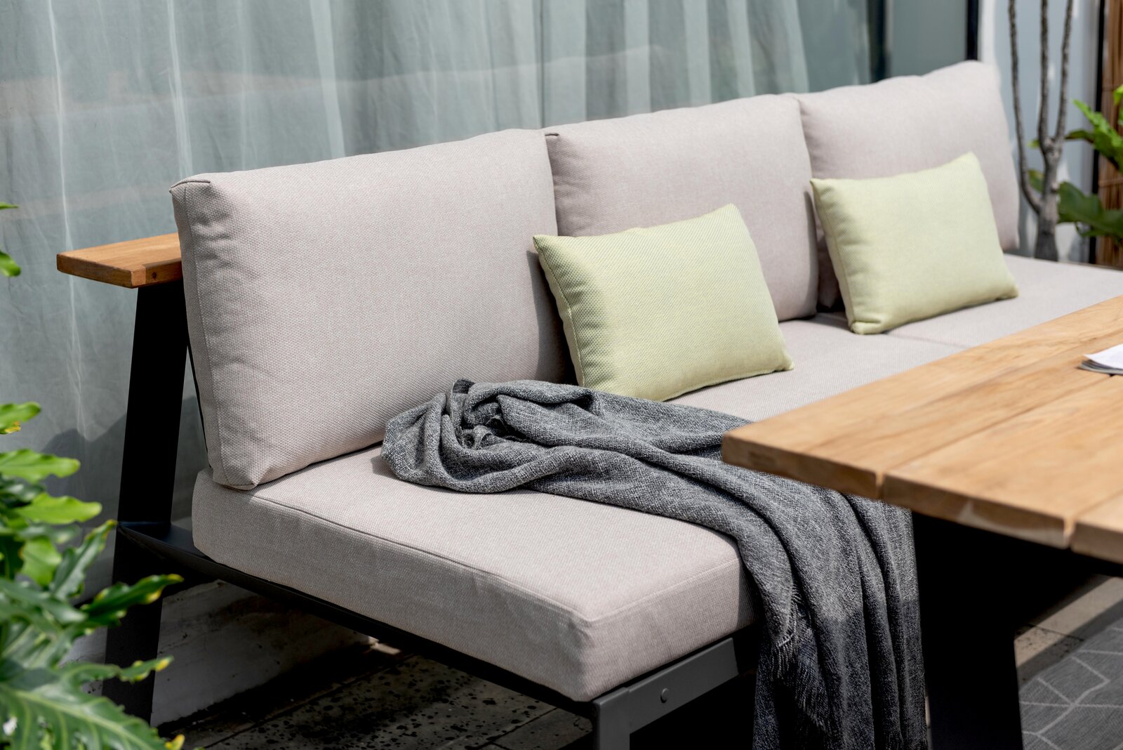 Gartensitzgruppe mit beiger Sitzbank, grünen Kissen und Holztisch, seitliche Perspektive