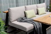 Gartensitzgruppe mit beiger Sitzbank, grünen Kissen und Holztisch, seitliche Perspektive