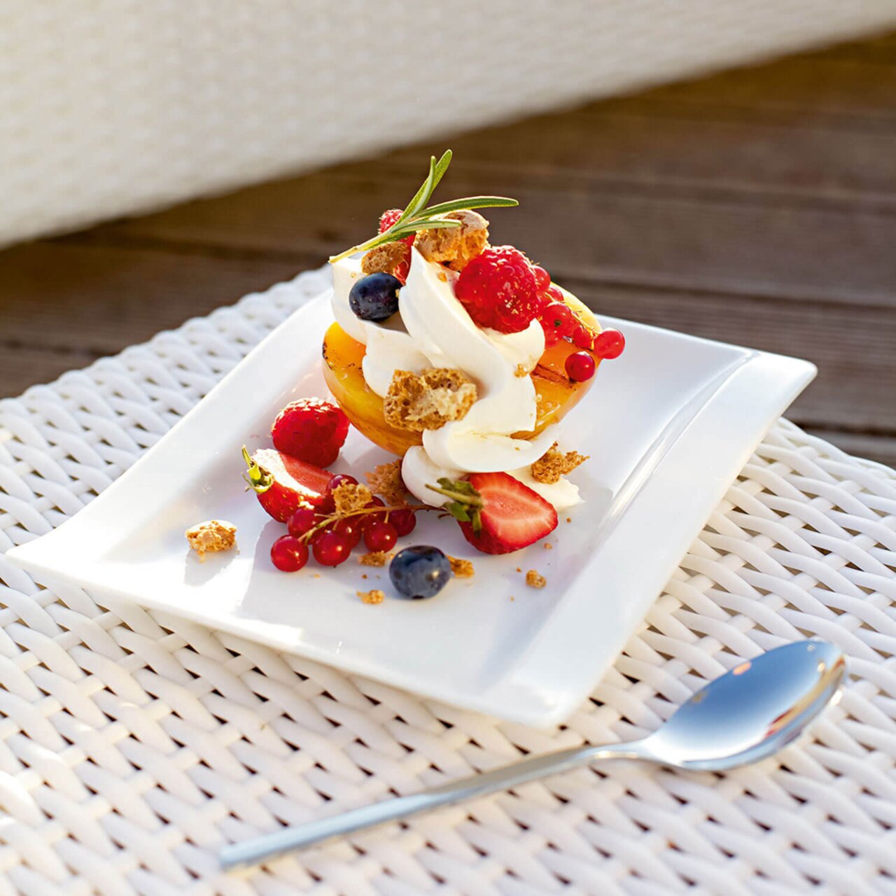 Rechteckiger Brotteller mit Dessert aus Sahne, Beeren und Keksstücken, von oben fotografiert.