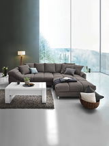 Moderne graue Rundecke in einem stilvollen Wohnzimmer mit großen Fenstern und Blick auf die Natur, aus der Vorderansicht fotografiert.