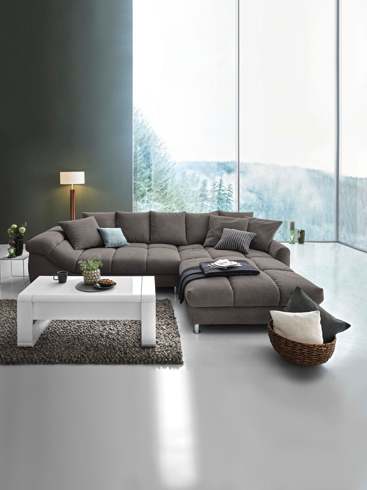 Moderne graue Rundecke in einem stilvollen Wohnzimmer mit großen Fenstern und Blick auf die Natur, aus der Vorderansicht fotografiert.